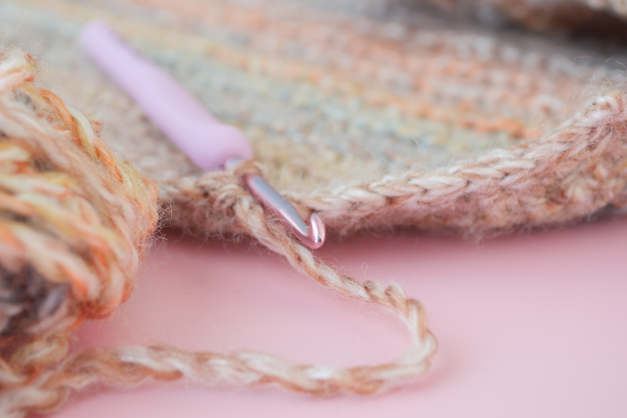 Closeup of a crochet hook and wool yarn on a magenta surface