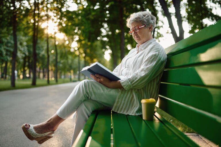 Mature woman reading a book on the bench in summer park
